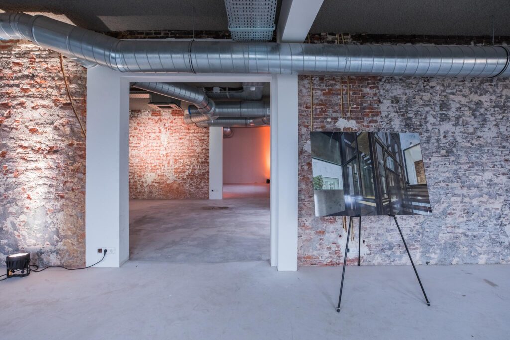 Industriële ruimte aan de Prins Hendrikkade met zichtbare bakstenen muren, ventilatiebuizen en een presentatiestandaard met architectuurvisualisatie.